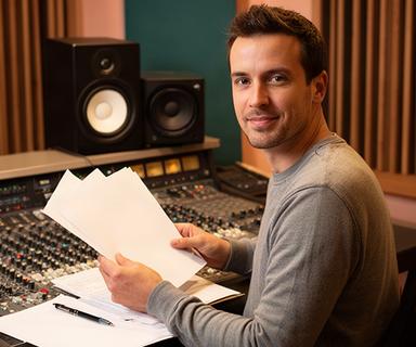 Lead podcast producer reviewing a radio script beside studio monitors